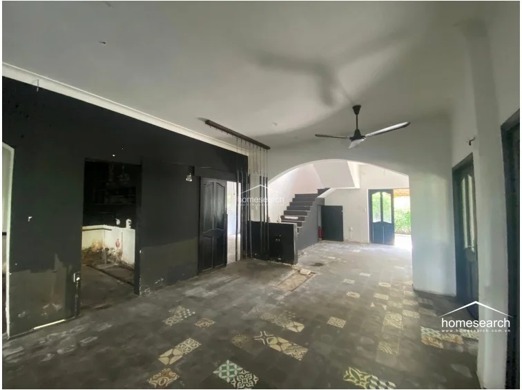 This interior living area features a bold, high-contrast color scheme with black accent walls and white ceilings, complemented by unique patterned floor tiles. The layout includes an open-plan design with a prominent archway leading to a staircase, creating a distinct architectural focal point and a sense of depth.