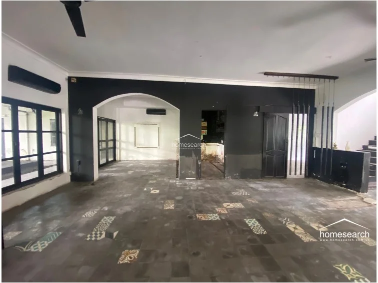 This spacious, open-plan interior features a bold aesthetic with matte black accent walls and a unique floor tiled with a mix of dark stone and decorative patterned inserts. The layout flows through large arched openings into adjacent rooms, while black-framed windows provide ample natural light and a view of the exterior. The ceiling is equipped with a modern fan, and the overall condition appears to be a well-maintained, contemporary commercial or high-end residential space.