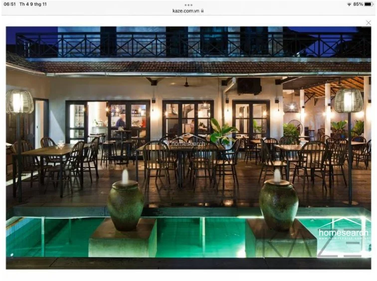 This elegant evening view highlights a sophisticated outdoor dining terrace featuring a tranquil water feature with illuminated fountains. The space is beautifully lit with warm ambient lighting, showcasing a well-maintained deck and a clear architectural transition into the interior living space.