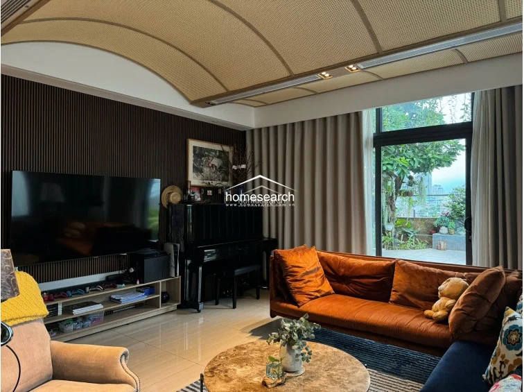 The space is furnished with a vibrant orange velvet sofa and a complementary navy blue sectional, creating a cozy yet modern seating arrangement around a marble-topped coffee table. A sleek black piano serves as a focal point against a dark, vertically-slatted feature wall, while the flooring consists of polished light-colored tiles that enhance the room's brightness.