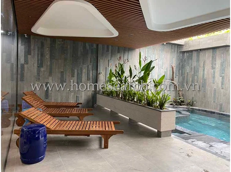This indoor lounge area features a sleek, modern design with dark stone-textured walls and a slatted timber ceiling. The space includes a private plunge pool and wooden sun loungers, creating a serene, spa-like atmosphere perfect for relaxation.