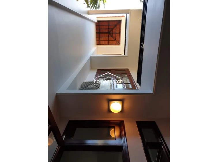 This view looks upward into an architectural light well or atrium, showcasing the vertical connection between the floors and the home's natural ventilation system. The space features dark wood window frames, an external AC unit, and a tiled roof section, reflecting a thoughtful design that maximizes light and airflow.