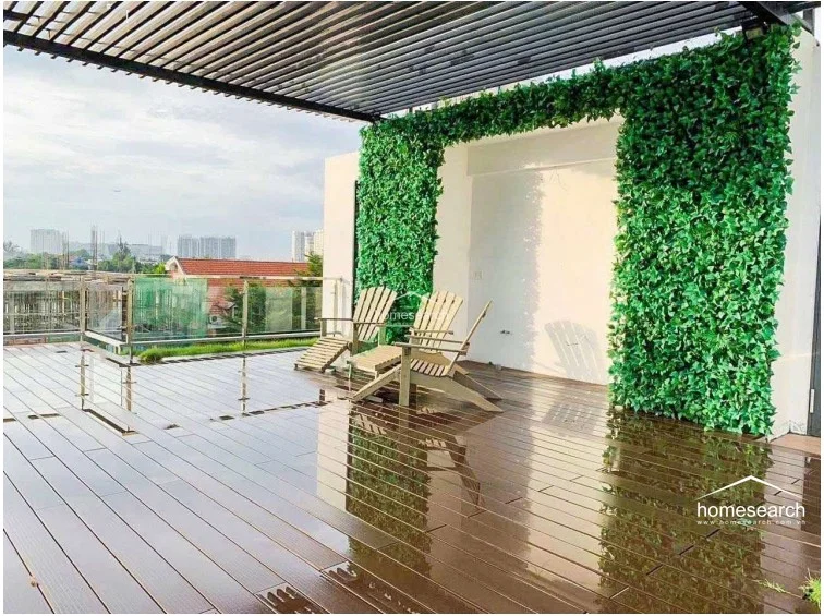 The terrace area is partially shaded by a modern slatted pergola, creating a comfortable transition between sun and shade. A decorative vertical garden wall adds a vibrant touch of nature to the minimalist white exterior, enhancing the overall aesthetic of this outdoor retreat.