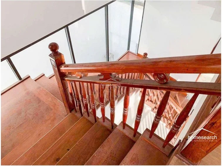 This interior staircase features rich, dark-toned wooden steps and a matching traditional balustrade with turned spindles. The design is complemented by modern floor-to-ceiling glass panels, creating a sophisticated contrast between classic woodwork and contemporary architectural elements.