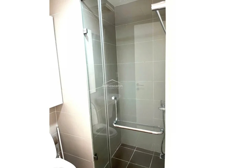 This bathroom features a walk-in shower enclosure with a glass door and polished chrome fixtures, set against neutral-toned wall and floor tiles. The space is compact and functional, with a wall-mounted toilet and a clean, well-maintained finish. The design prioritizes efficiency and modern simplicity in its layout.