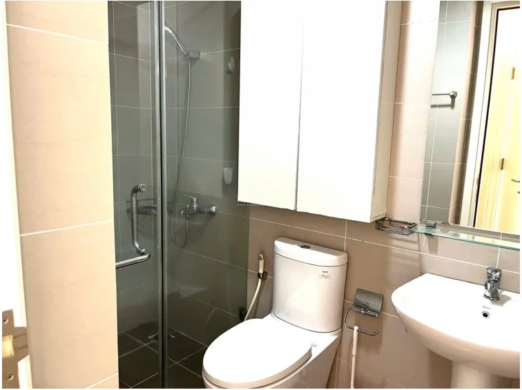 The bathroom is efficiently designed with a glass-enclosed walk-in shower and a wall-mounted medicine cabinet for added storage. It features neutral-toned wall tiles, a pedestal sink, and a clean, well-maintained finish that maximizes the compact floor plan.