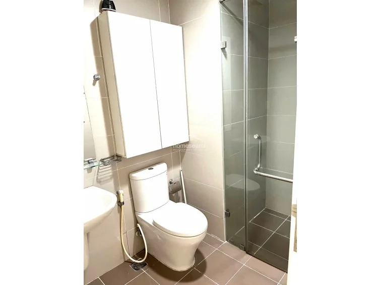 This compact bathroom features a modern glass-enclosed shower stall and neutral beige tile flooring and wall finishes. It is equipped with a wall-mounted storage cabinet above the toilet and a pedestal sink, presenting a clean and well-maintained appearance.