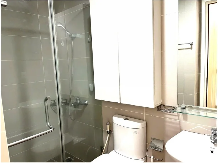 This modern bathroom is finished in neutral, large-format wall tiles and includes a glass-enclosed walk-in shower. It is well-equipped with a white vanity, a wall-mounted storage cabinet, and high-quality fixtures, reflecting a well-maintained and functional design.
