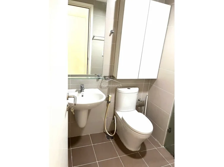 The bathroom is finished with neutral-toned wall tiles and darker floor tiles, featuring a standard pedestal sink and a modern white toilet. A large wall-mounted storage cabinet provides essential utility, and the space appears to be in well-maintained, clean condition.