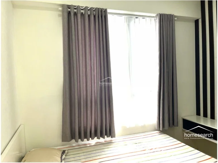 This view highlights the bedroom's window, which is dressed with floor-to-ceiling grey curtains that provide privacy and effective light control. The window allows for ample natural light, brightening the space and complementing the neutral color palette.