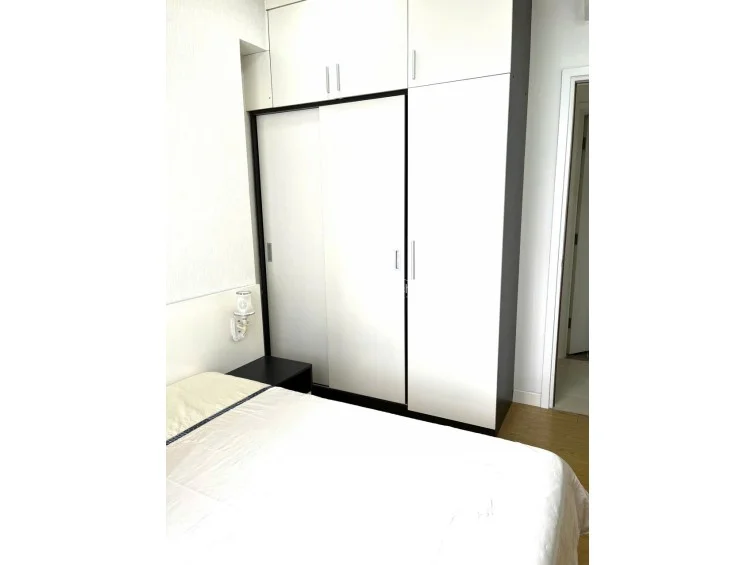 This bedroom includes a floor-to-ceiling white wardrobe with sliding doors, providing excellent built-in storage capacity. The room features light wood-look flooring and a minimalist design, maintaining a tidy and well-maintained appearance.