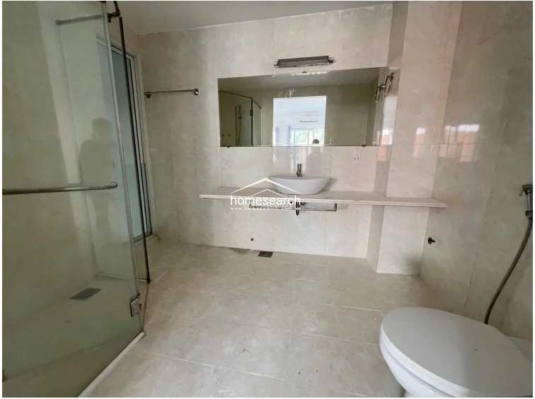 This bathroom features a spacious, modern design with floor-to-ceiling beige marble-look tiles and a large vanity mirror. It is equipped with a contemporary vessel sink, a glass-enclosed walk-in shower, and high-quality fixtures, reflecting a high level of maintenance and a clean, spa-like finish.