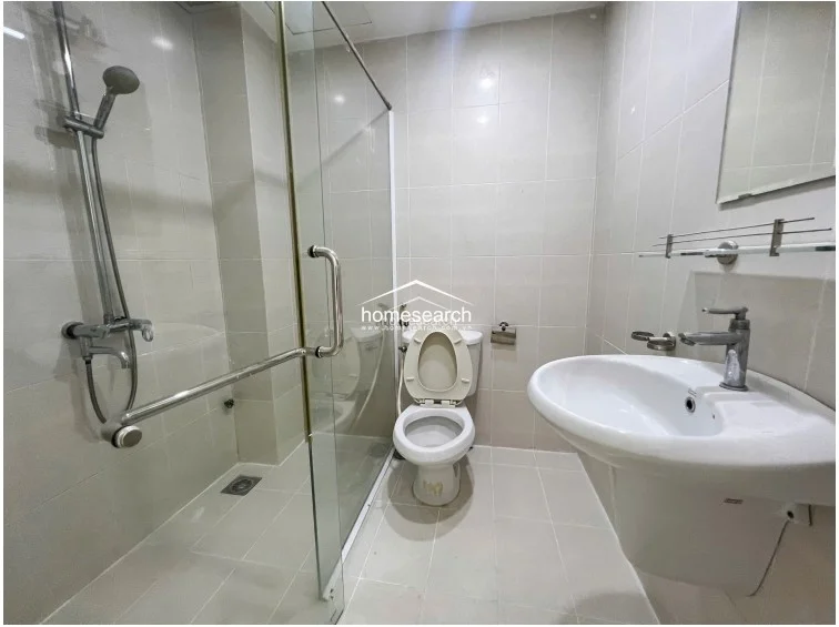 This modern bathroom is equipped with a glass-enclosed walk-in shower and a pedestal sink with a glass shelf above. The space is fully tiled in a neutral palette, presenting a clean, well-maintained, and contemporary aesthetic.