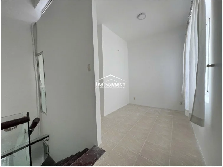 This area appears to be a landing or transition space, featuring light-colored tile flooring and white walls. It connects directly to a staircase with a modern glass and dark wood railing, and includes a small window that provides natural light to the stairwell.