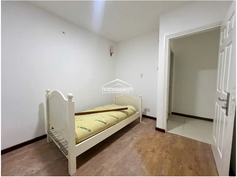 This secondary bedroom is compact and functional, featuring a single bed with a white frame and light wood-tone flooring. The room is finished with plain white walls and provides a simple, neutral space that connects directly to an adjacent hallway.