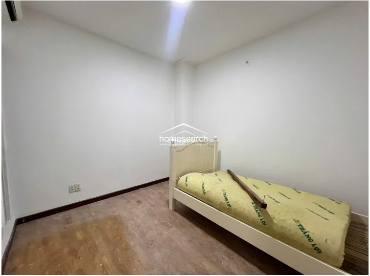 This minimalist bedroom is designed for simplicity, featuring a single bed with a white frame and light wood-tone flooring. The room maintains a clean, uncluttered look with plain white walls and basic electrical outlets, offering a versatile space for a guest room or study.