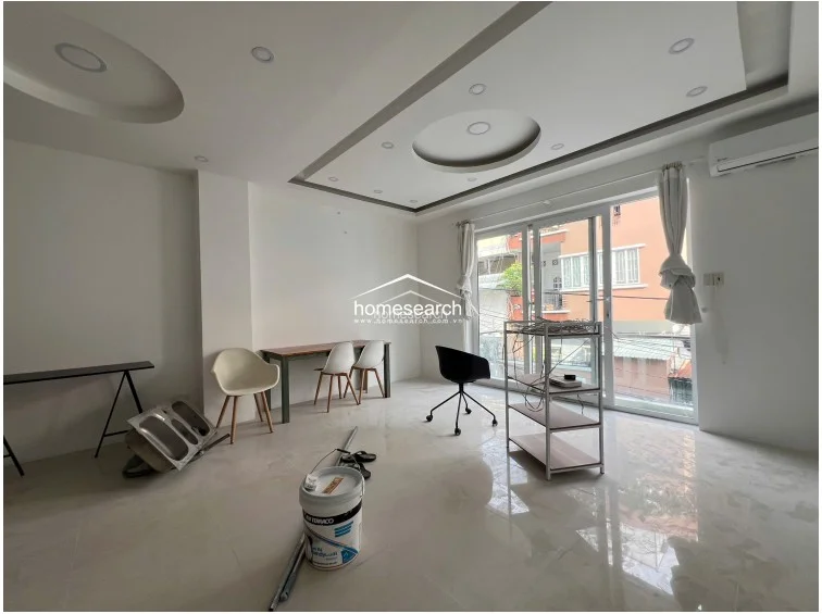 This bright living area features a sophisticated recessed ceiling with circular light fixtures and a wall-mounted air conditioning unit. The space is finished with polished light-colored tile flooring and large glass doors that provide access to an outdoor balcony.