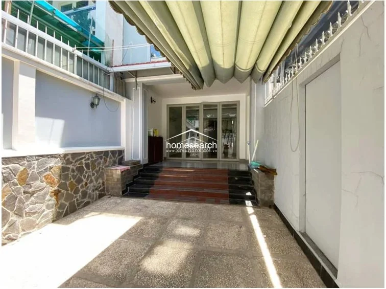 The courtyard view from the interior entrance highlights the transition between the outdoor space and the living area via a set of wide, tiled steps. The area is protected by a retractable canopy and features clean, white-painted walls, suggesting a tidy and practical outdoor utility or parking zone.