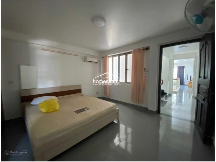 This bedroom is identical to the previous image, showcasing a clean and well-maintained space with a double bed and a simple wooden headboard. The layout allows for easy flow into the adjacent hallway, which provides a glimpse into the rest of the home's interior, maintaining a consistent, modest aesthetic throughout.