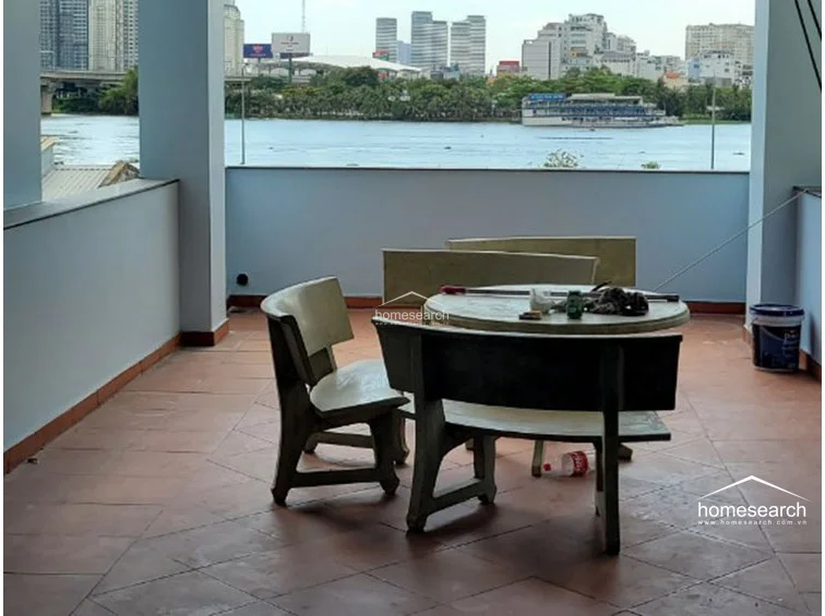 This spacious outdoor terrace offers a panoramic waterfront view of the city skyline, providing an ideal setting for relaxation or outdoor dining. The area is paved with terracotta-style tiles and furnished with a sturdy stone table and bench set, creating a functional and open-air living space.