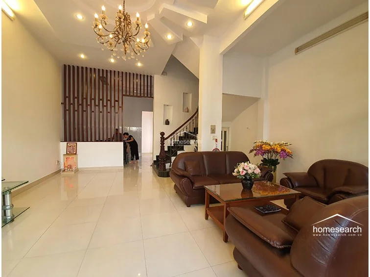 This open-concept living area maintains a consistent design language with white walls and glossy tile floors, emphasizing a sense of depth and openness. A decorative wooden slat partition provides a subtle visual divider between the living space and the rear of the home, while a traditional altar adds a touch of cultural detail.