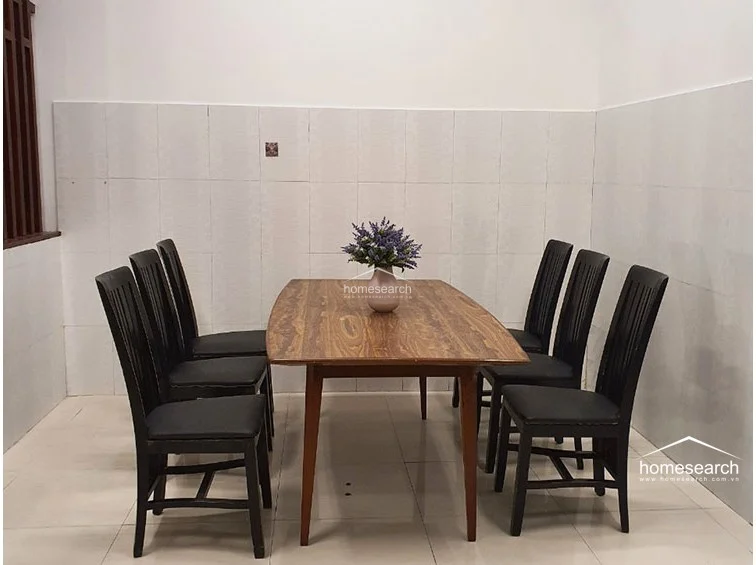 The dining area is simple and functional, featuring a polished wooden dining table paired with six black chairs. The walls are partially finished with white ceramic tiles, which offer a practical and easy-to-clean surface, while the open flow suggests a connection to the rest of the ground floor living space.