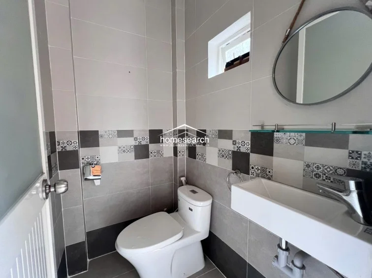 This compact powder room features a modern, minimalist design with a wall-mounted rectangular basin and a sleek, round mirror. The walls are finished in a contemporary mix of light gray, dark gray, and patterned decorative tiles, providing a clean and stylish aesthetic.