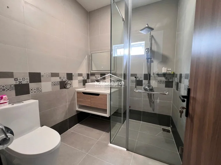 This contemporary bathroom is equipped with a glass-enclosed walk-in shower and a wall-mounted vanity with a wooden cabinet. The space is finished in neutral-toned tiles with a decorative accent band, and it includes a small window that provides natural light and ventilation.