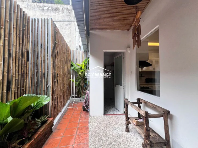 This private outdoor terrace features terracotta floor tiles and a bamboo privacy screen, creating a serene, natural atmosphere. It includes a rustic wooden bench and direct access to the interior, with lush potted plants adding a touch of greenery to the space.