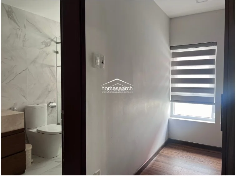 This bathroom is finished with high-quality marble-style wall tiles and features a sleek, modern vanity with a dark wood cabinet. The space includes a glass-enclosed shower area and a window with adjustable blinds, maintaining a clean and well-maintained aesthetic.