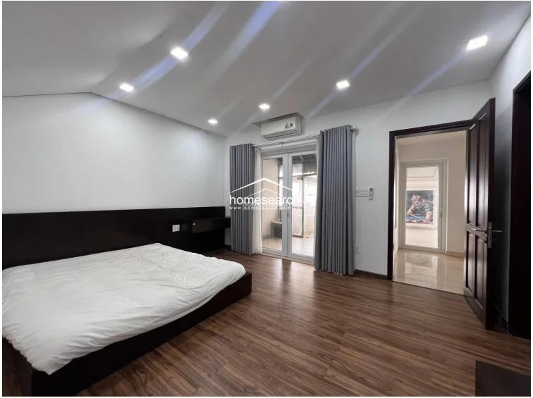 This bedroom layout provides a seamless transition to an outdoor terrace through double glass doors, enhancing the sense of space and natural light. The room is furnished with a dark wood bed frame and low-profile media console, complemented by recessed ceiling lights and neutral wall tones.