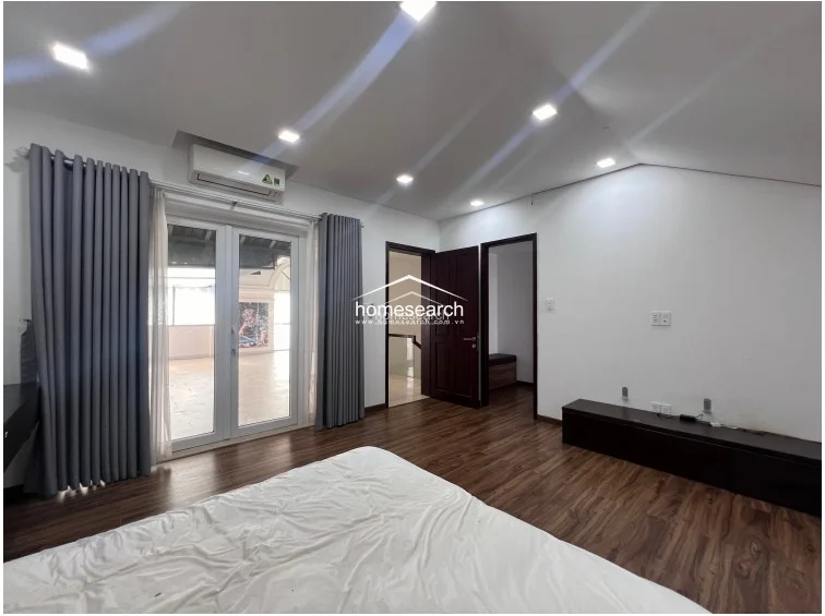 This bedroom view highlights the functional layout, showing the connection to the hallway and the terrace access point. The room features durable wood-laminate flooring, a wall-mounted AC unit, and a minimalist design scheme that maximizes the available floor space.
