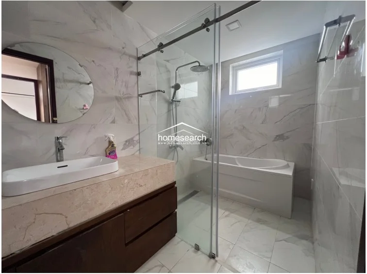This modern bathroom features sleek white marble-look wall and floor tiles, creating a bright and clean aesthetic. It is equipped with a contemporary vessel sink on a stone vanity, a frameless glass-enclosed shower area, and a separate deep soaking tub positioned under a small window for natural light.
