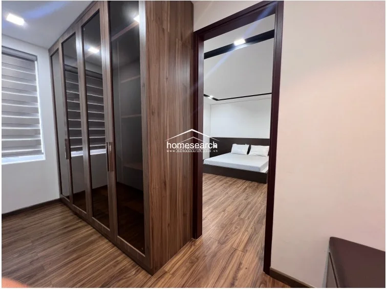 This functional dressing area or transition space is equipped with a floor-to-ceiling wardrobe featuring dark wood frames and glass panel doors. It provides a seamless flow into the adjacent bedroom, maintaining the consistent wood flooring and neutral wall palette found throughout the suite.