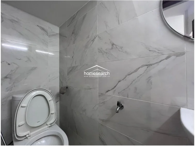 This compact powder room or secondary bathroom is finished with high-quality white marble-veined tiles that extend from floor to ceiling. It includes a modern white toilet and a minimalist chrome faucet fixture, reflecting a clean, contemporary, and well-maintained interior design.