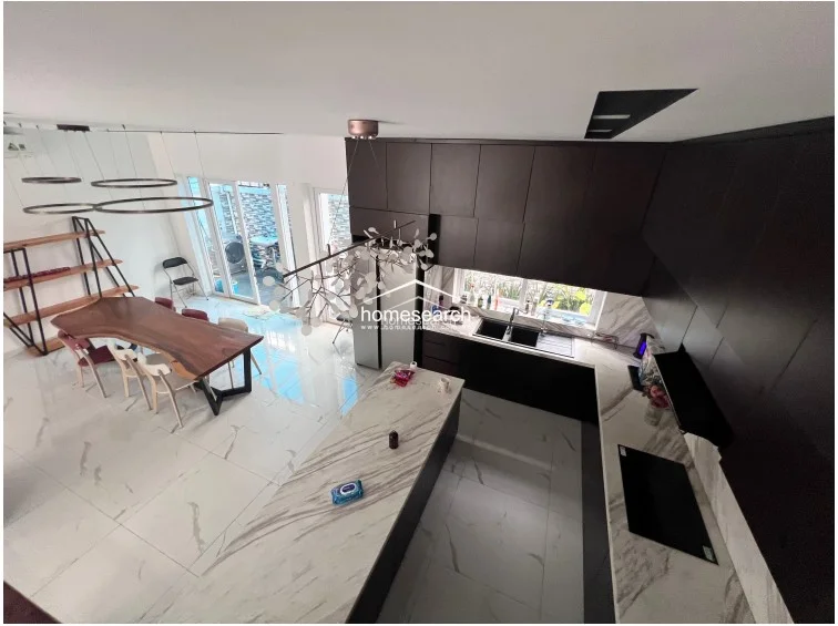 This high-angle view highlights the kitchen's efficient U-shaped layout, which includes a spacious marble island and integrated appliances. The open floor plan connects the kitchen directly to the dining area and a rear outdoor terrace, emphasizing a functional and modern living flow.