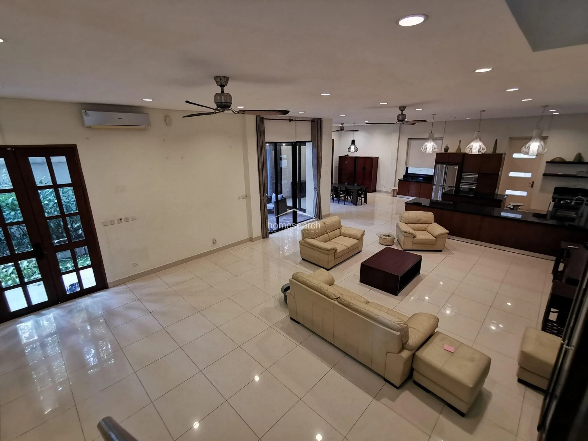 This expansive open-concept living and dining area features polished light-colored tile flooring and a neutral color palette, creating a bright and airy atmosphere. The space is well-equipped with ceiling fans, recessed lighting, and a modern kitchen with dark cabinetry and a breakfast bar, while large glass doors provide direct access to an outdoor balcony.
