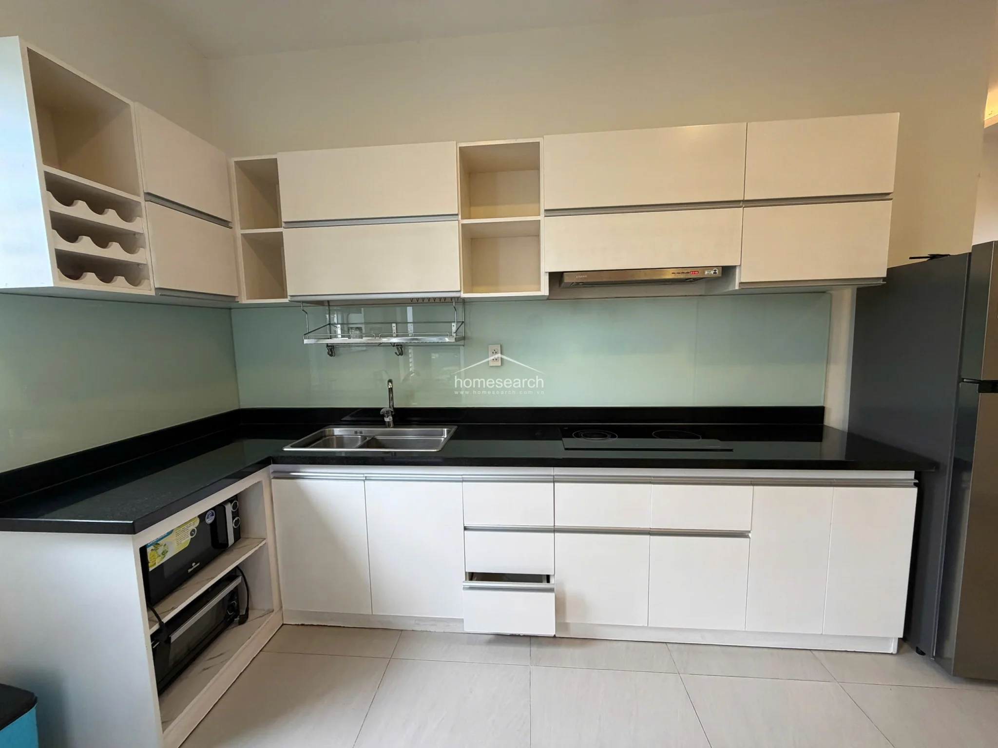 This close-up of the kitchen showcases high-quality finishes, including modern white cabinetry with ample storage and a dedicated wine rack. The sleek black countertop contrasts well with the light-colored tile flooring, and the space is maintained in excellent condition with integrated appliances.