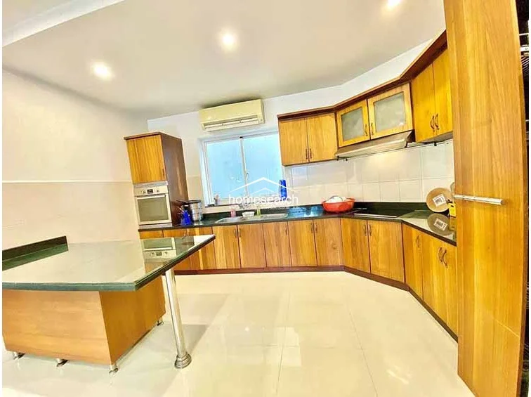 The kitchen boasts a functional U-shaped layout with warm-toned wooden cabinetry, contrasting dark countertops, and a convenient breakfast bar island. It is well-equipped with a built-in oven and ample storage, while a wall-mounted AC unit ensures comfort in this high-traffic space.