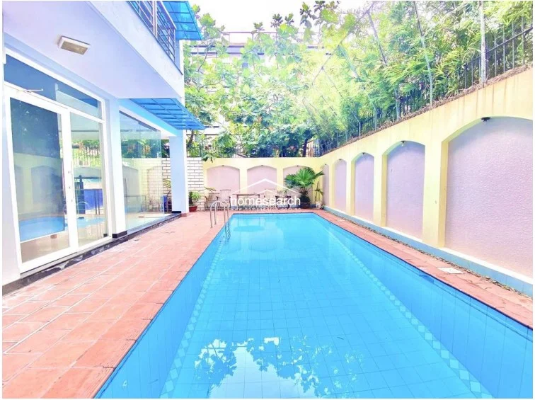 This perspective highlights the seamless transition between the indoor living area and the outdoor pool, emphasizing the property's focus on natural light and ventilation. The pool is framed by a high perimeter wall with architectural arches, providing a private and tranquil setting for outdoor relaxation.