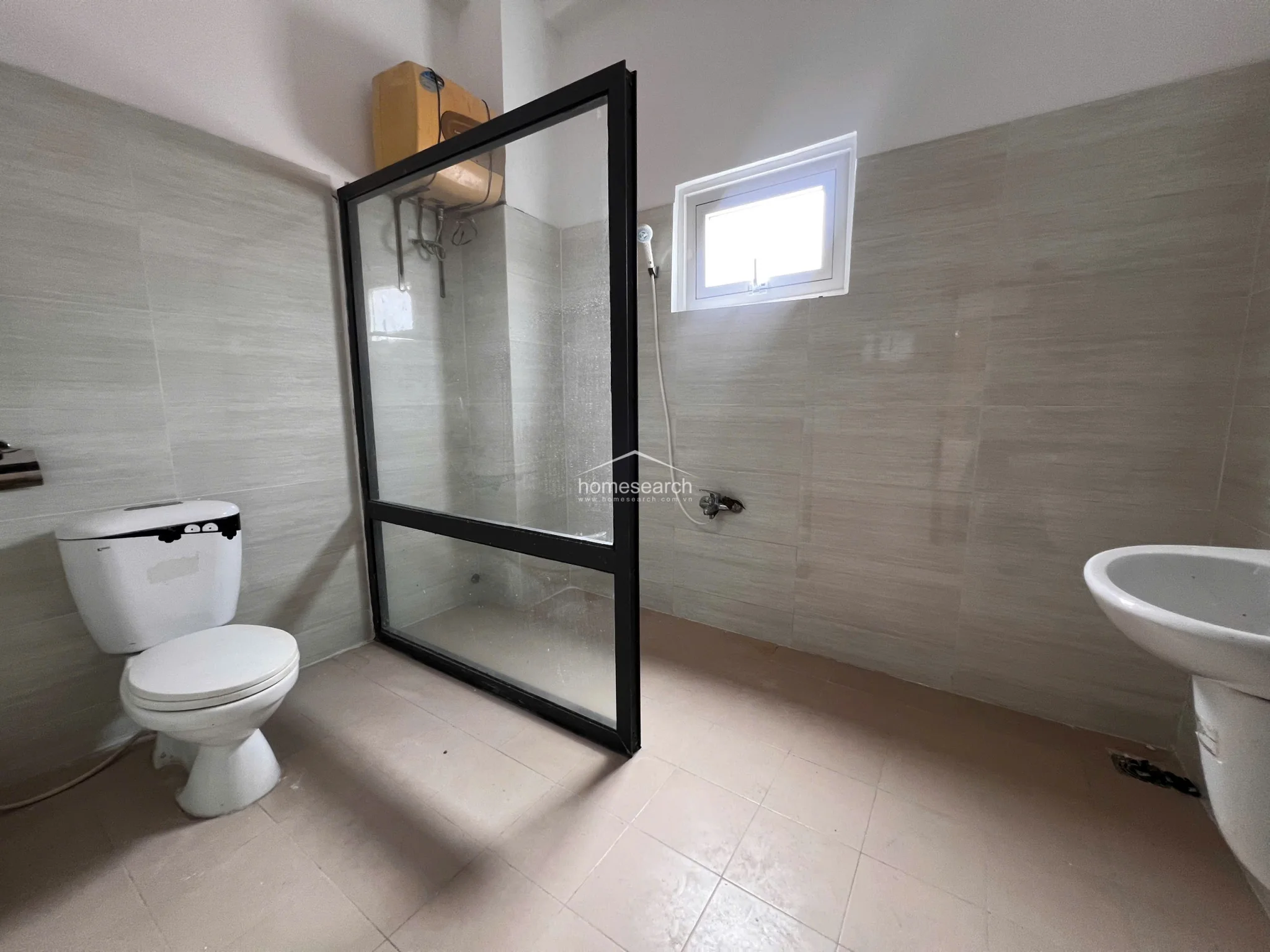 This bathroom features a walk-in shower enclosure with a sleek black frame and light-toned wall tiles. It is equipped with a standard white toilet, a pedestal sink, and a wall-mounted water heater, presenting a clean and functional design.