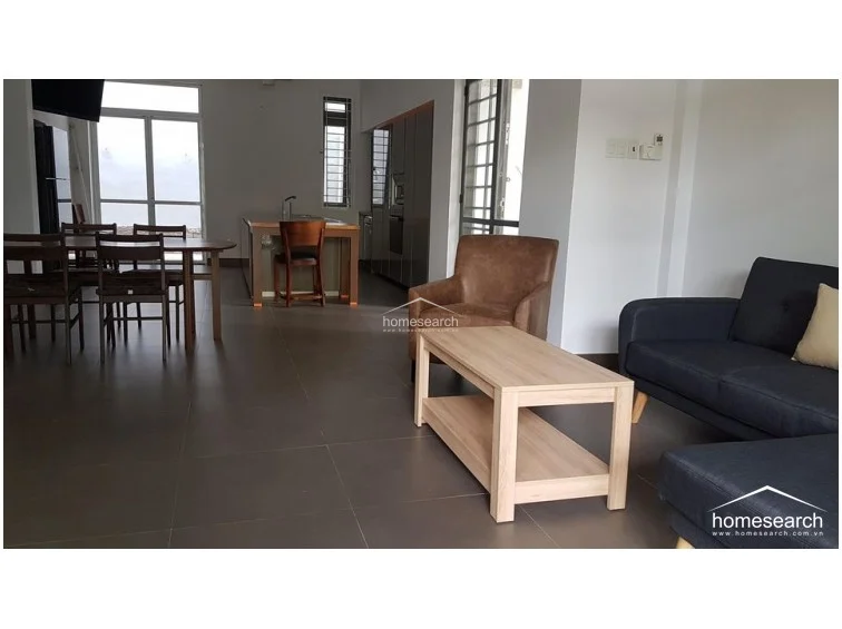 This view highlights the cohesive open-plan living area, where the dark grey sofa and warm brown armchair create a comfortable seating zone adjacent to the dining space. The neutral color palette, combined with the consistent tile flooring and modern furniture, creates a sophisticated and airy atmosphere throughout the home.