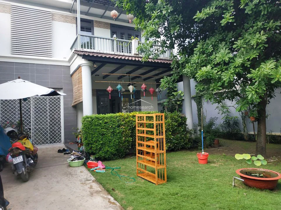 The property exterior highlights a spacious driveway and a well-maintained lawn, providing ample room for parking and outdoor activities. The house features a modern aesthetic with grey tiled accents, a balcony with railings, and a covered terrace area, reflecting a well-kept and inviting residential structure.
