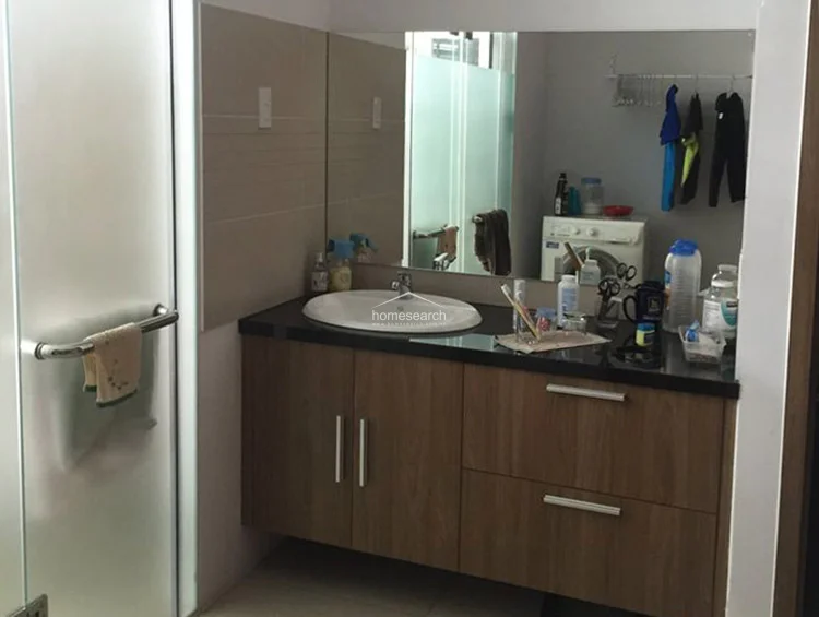 This bathroom is equipped with a functional, wall-mounted vanity unit that maximizes floor space and provides essential storage. The neutral color scheme and large mirror create an illusion of depth, though the presence of laundry equipment indicates that the space is currently being utilized as a combined bathroom and laundry area.