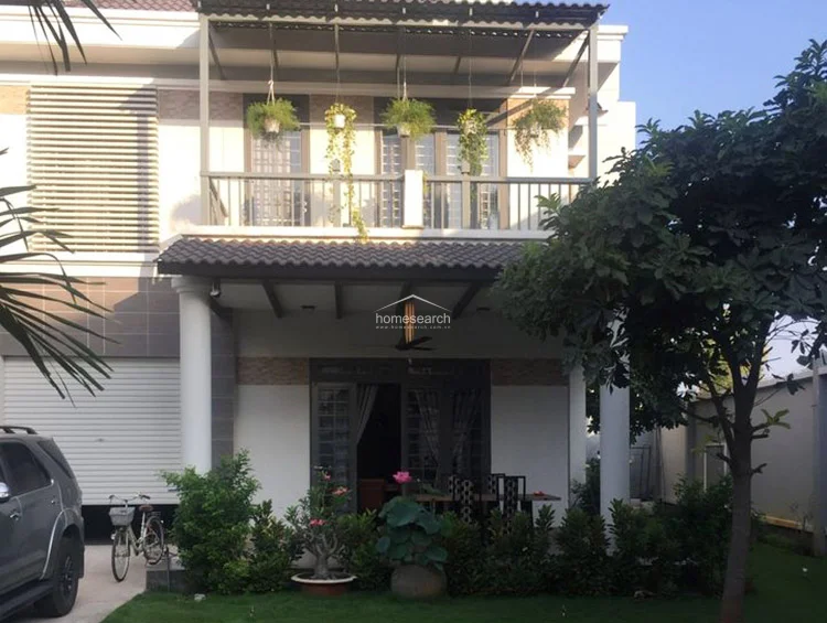 This view highlights the home's facade, emphasizing the integration of indoor and outdoor living spaces through a large sliding glass door. The upper balcony is adorned with hanging plants, adding a vibrant green touch to the clean, modern structure.