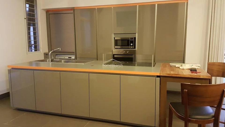 This modern kitchen features sleek, high-gloss grey cabinetry with a contrasting orange trim and a functional island layout. It is equipped with integrated appliances, including an oven and microwave, and features a clean, minimalist design with tiled flooring.