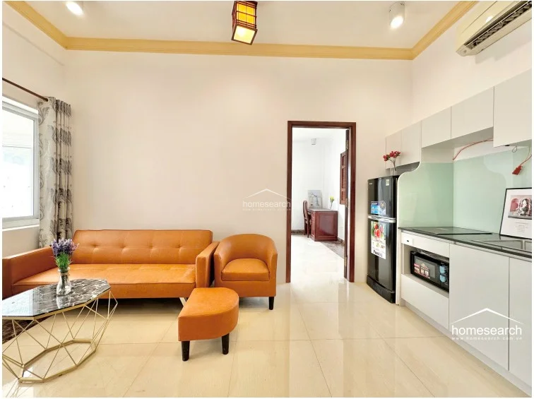This view highlights the seamless transition between the living room and the bedroom, emphasizing the functional, compact floor plan. The kitchen area remains visible in the background, showcasing the cohesive design and the well-maintained, bright interior space.