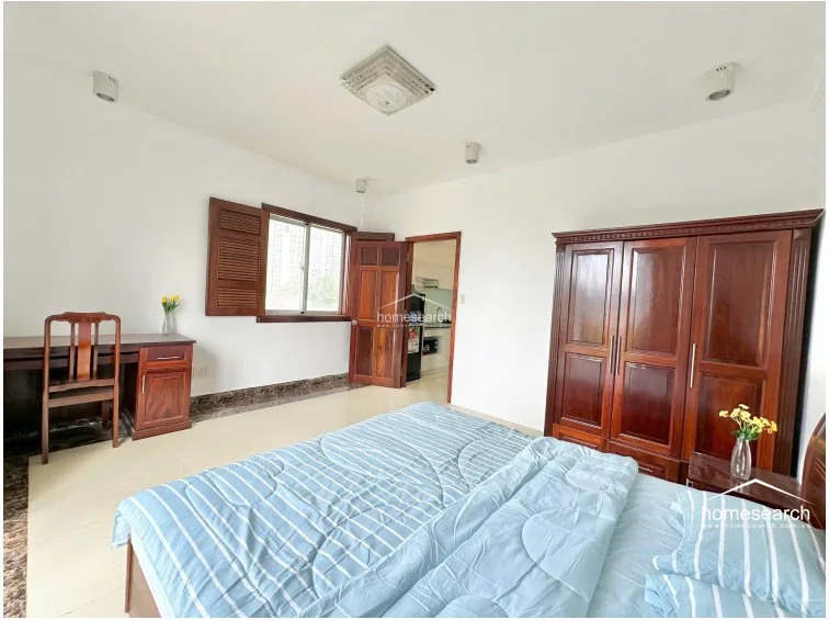 This bedroom layout includes a dedicated wooden desk area positioned under a window with classic wooden shutters, offering a functional workspace. The room maintains a consistent design language with the rest of the home, featuring high-quality wooden furniture, recessed ceiling lighting, and a clean, well-kept appearance.