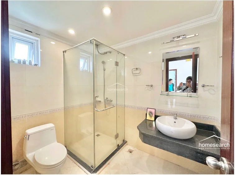 This bathroom layout mirrors the previous one, showcasing a clean and well-maintained design with a glass-enclosed shower, a white vessel sink, and a wall-mounted mirror. The neutral tile work and granite vanity provide a polished look, while the small window ensures the space remains bright and airy. The overall condition is excellent, reflecting consistent maintenance.