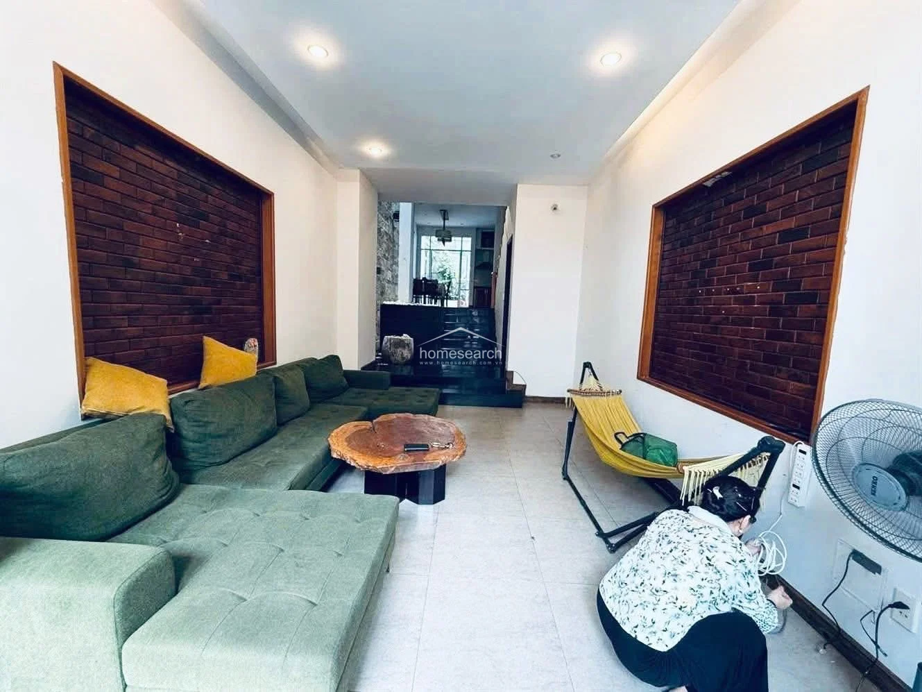 The reverse angle highlights the spaciousness of the living area, which transitions seamlessly into a rear dining and kitchen zone. The room is well-maintained, featuring recessed ceiling lighting, a portable hammock for relaxation, and a standing fan for climate control.